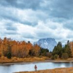 Angler casting a fly rod in a Wyoming river, surrounded by scenic landscape