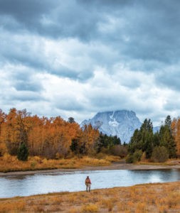 Angler casting a fly rod in a Wyoming river, surrounded by scenic landscape