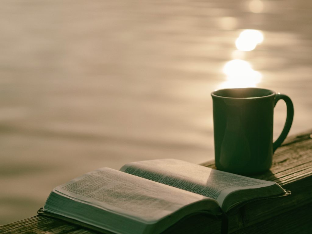 Open Bible and coffee cup by a lakeside, illustrating guided meditation and contemplation of scripture.