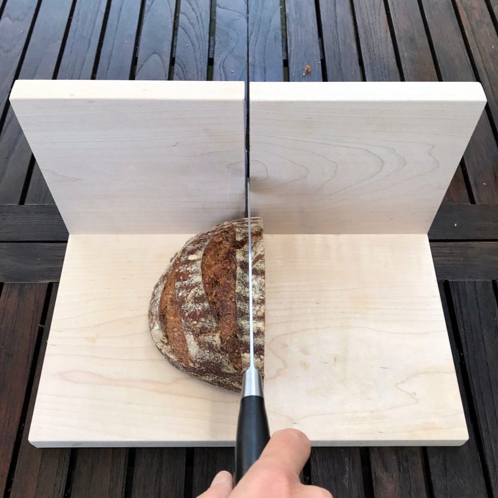 Close-up view of the homemade wooden bread slicer guide holding a sourdough loaf, showcasing its design and functionality