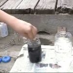 Close-up of hands using tongs to dye a yoyo half in a glass jar with colored liquid