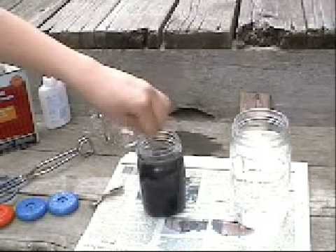 Close-up of hands using tongs to dye a yoyo half in a glass jar with colored liquid