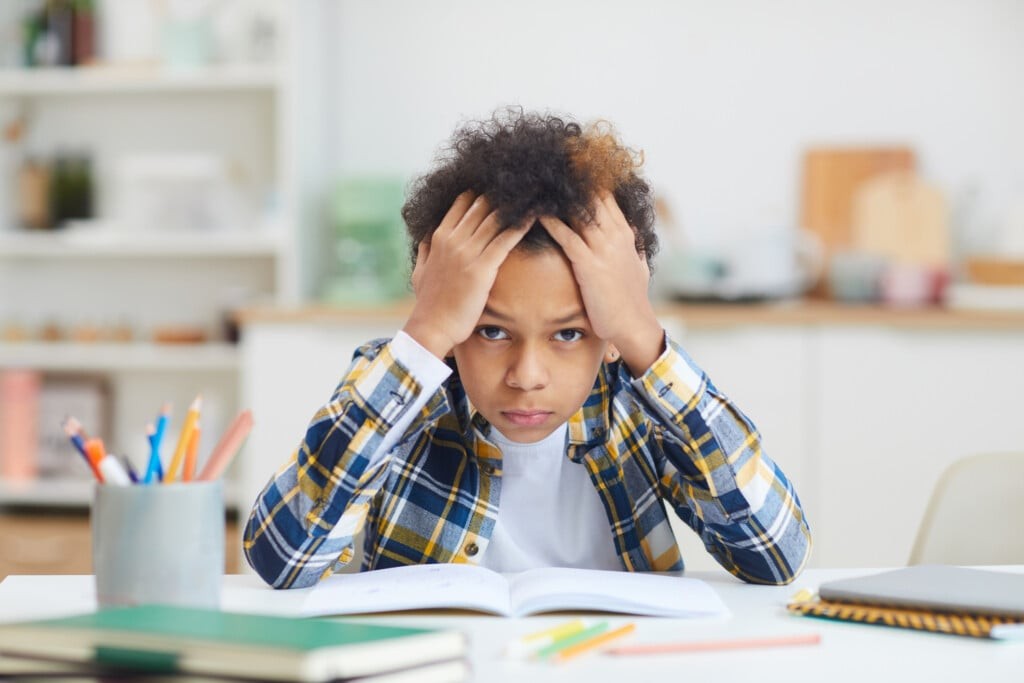 Stressed child with homework, symbolizing the pressures of overparenting and academic anxiety