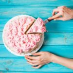 Close-up of a slice being expertly removed from a round cake decorated with delicate pink buttercream rosettes