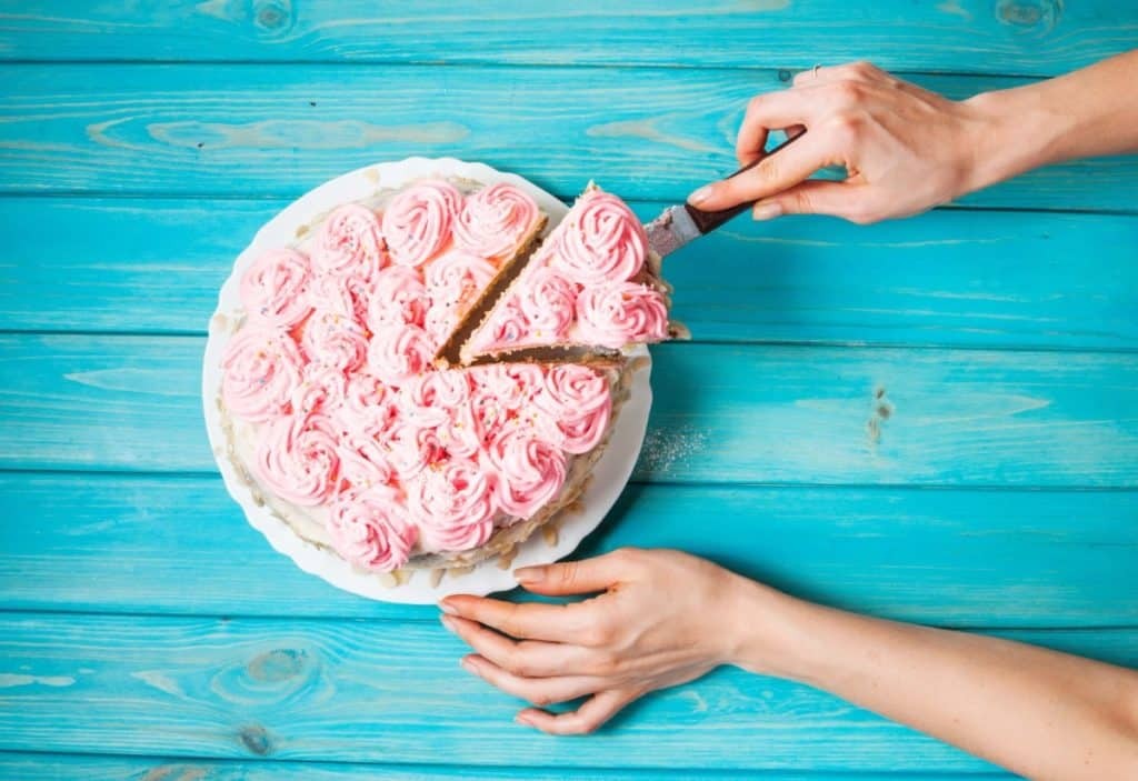 Close-up of a slice being expertly removed from a round cake decorated with delicate pink buttercream rosettes