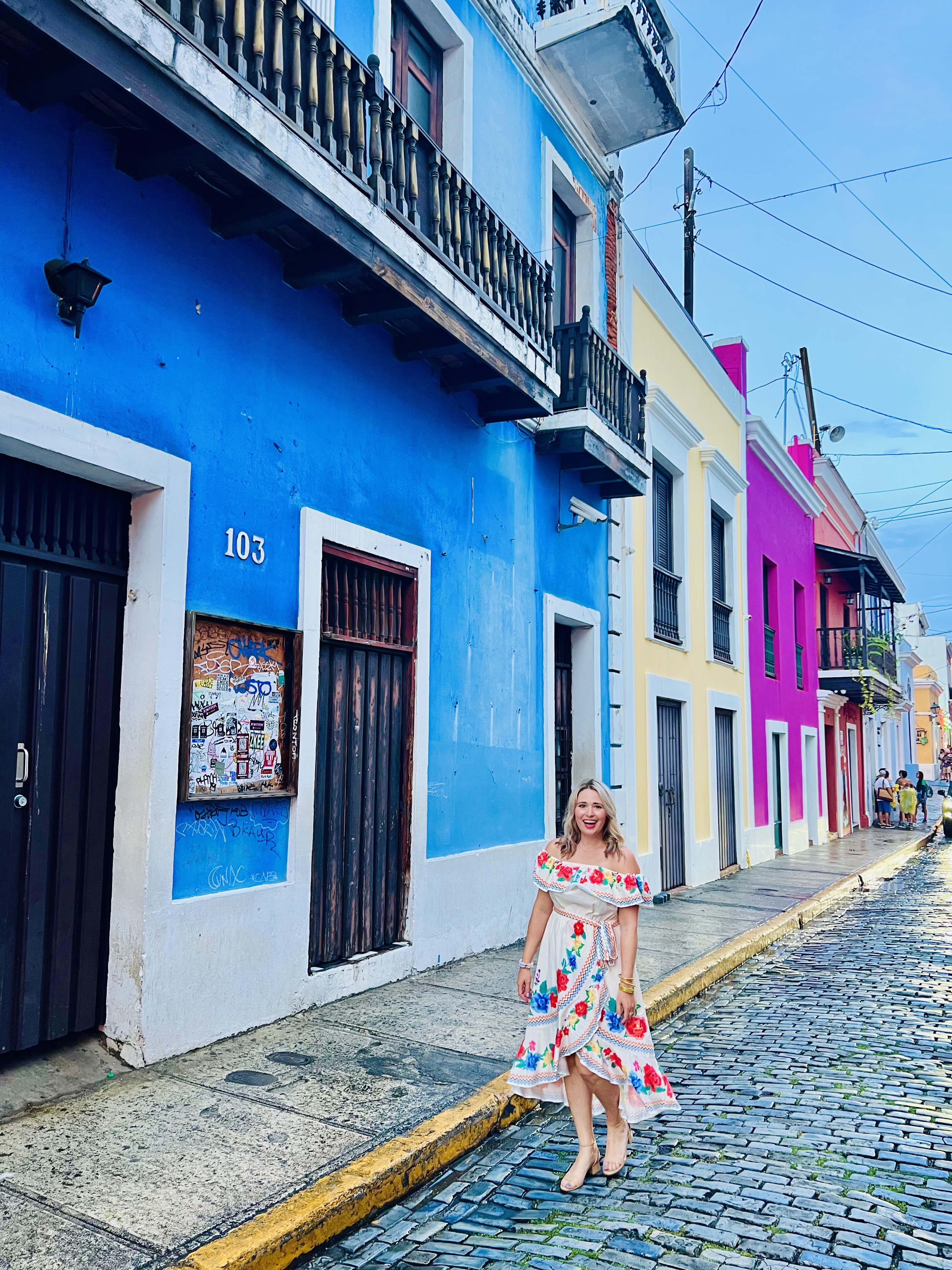 A narrow street in Old San Juan lined with brightly colored buildings and blue cobblestone streets