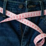 Man measures his waist with a measuring tape to determine his pants size.