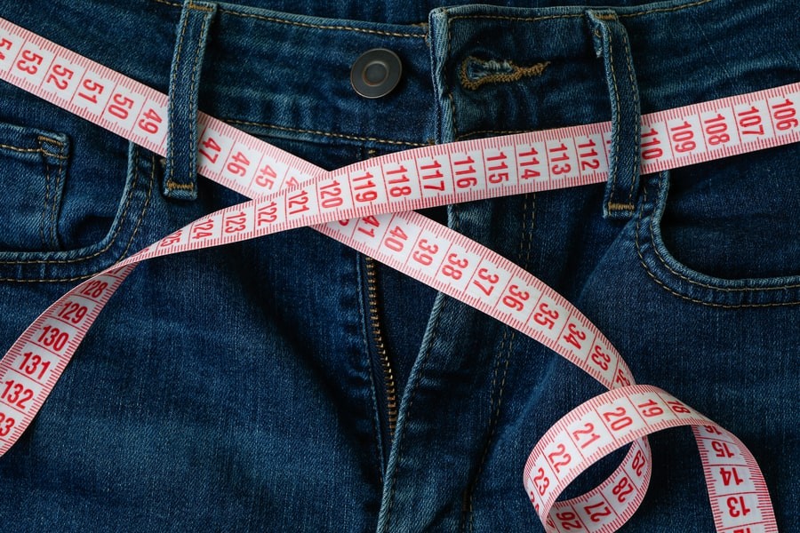 Man measures his waist with a measuring tape to determine his pants size.