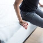 A tester sits on the edge of a foam mattress