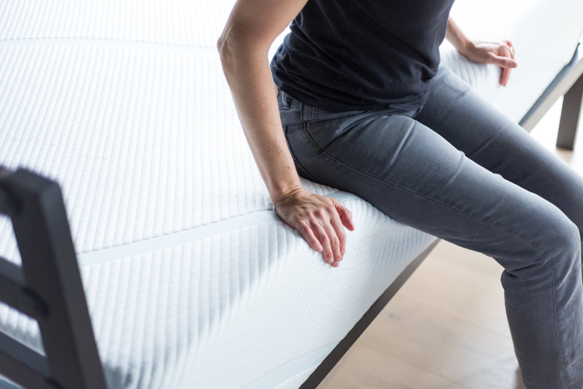 A tester sits on the edge of a foam mattress