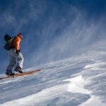 A skier in bright orange jacket and ski pants skiing on a snowy mountain slope.