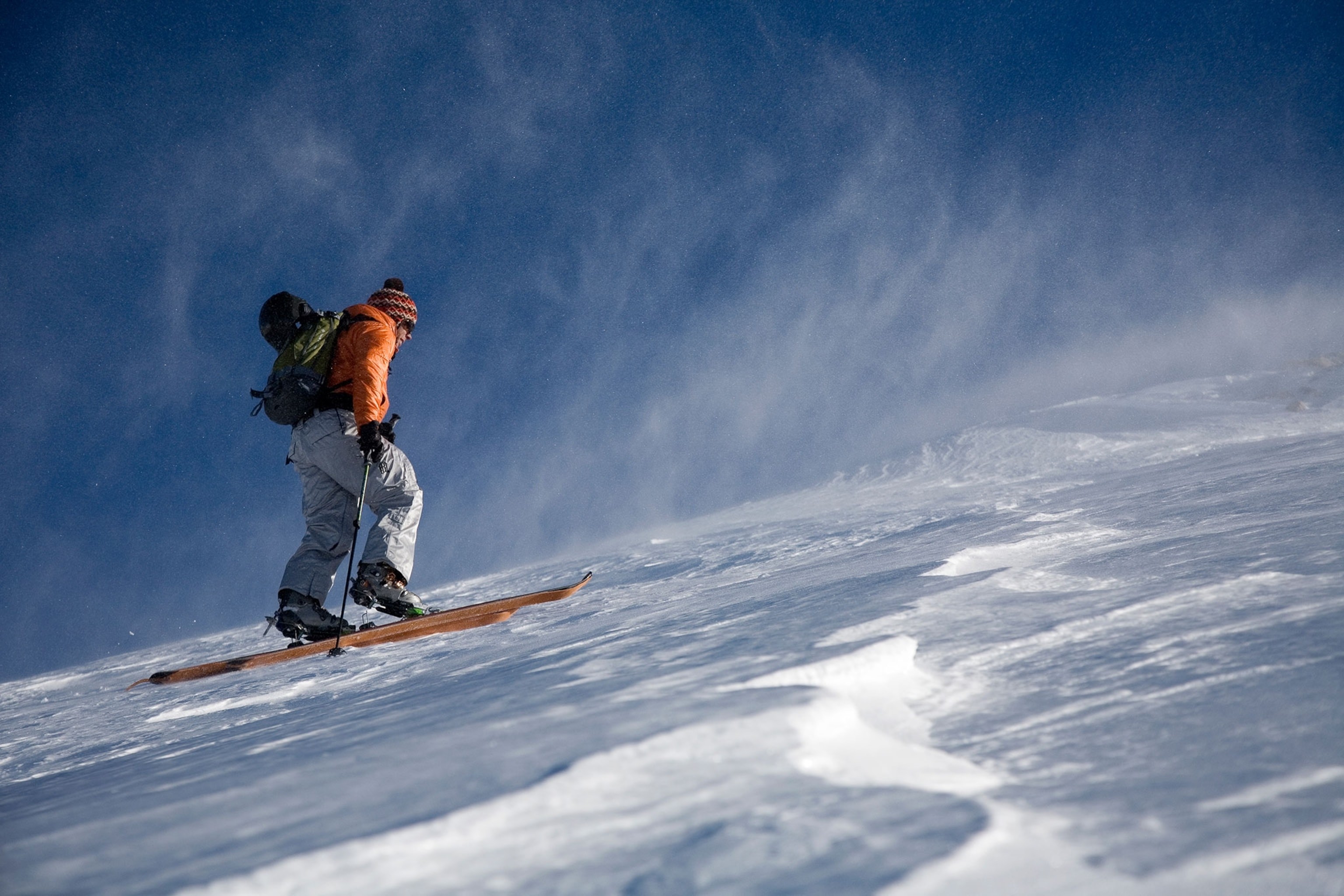 A skier in bright orange jacket and ski pants skiing on a snowy mountain slope.