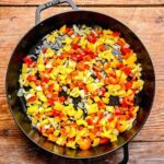 Sautéing diced bell peppers and yellow onions in a pan for spicy chicken chipotle pasta.