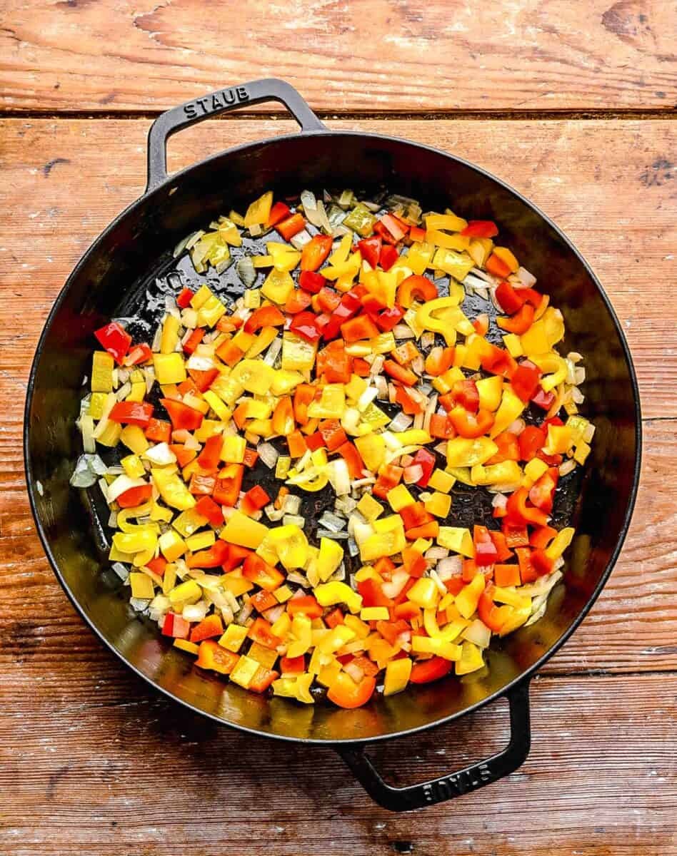 Sautéing diced bell peppers and yellow onions in a pan for spicy chicken chipotle pasta.