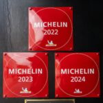 Three square red signs read Michelin 2022, Michelin 2023, and Michelin 2024 on a restaurant door frame.