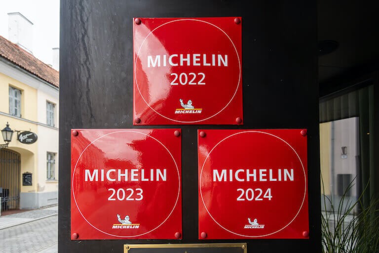 Three square red signs read Michelin 2022, Michelin 2023, and Michelin 2024 on a restaurant door frame.