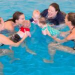 Three parents with their babies and a swim teacher in a Water Babies class