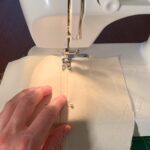 A close-up of a sewing machine being used to make a flat-felled seam, down the middle of a piece of fabric.