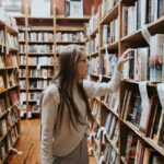 Woman engrossed in a book, surrounded by towering bookshelves